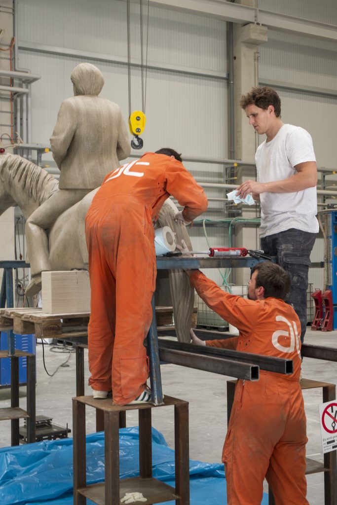 workers in factory assembling 3d prin of angela merkel equestrian